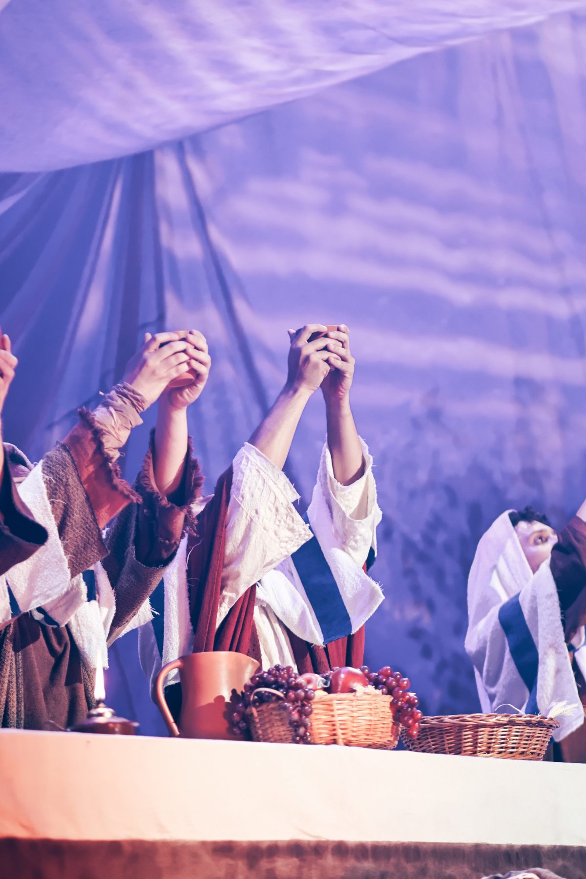 Mãos erguidas segurando taças em cena de encenação teatral, iluminação roxa
